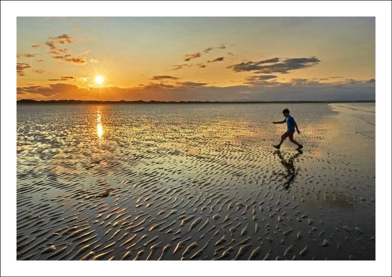 A boy dances on the sand as the sun sets over the Old Course, St Andrews West Sands.